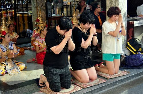 Three devout Buddhist Thais kneel in prayer in front of a group of seated Khong dancers at the revered Erawan Shrine in Bangkok, Thailand. Thailand people stock images, royalty-free photos and pictures