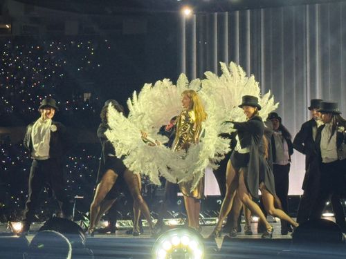 Swift onstage in the middle of her backup dancers, all shaking their hands in the air