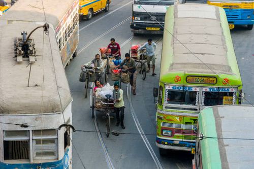 Cyclists between busses and a tram on a busy road in the suburb Sealdah.