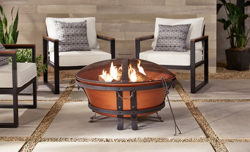 A cast iron fire pit with a copper finish on a patio with outdoor furniture.