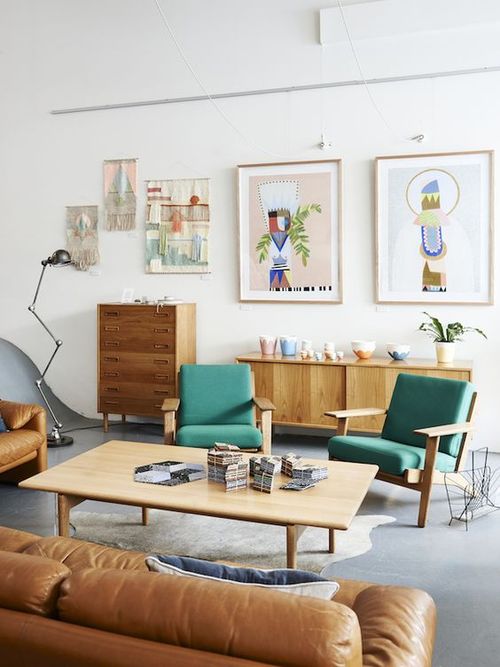 A bright mid-century modern living room with stained furniture, green chairs, an amber leather sofa, a low coffee table, a gallery wall and beautiful potted plants.