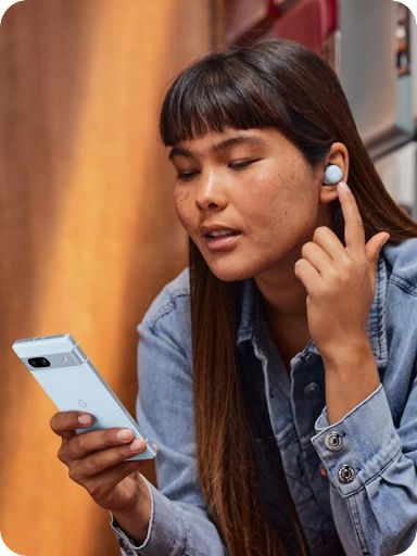 An Android user is holding a conversation, touching their earbud with their finger and looking down at their Android phone.