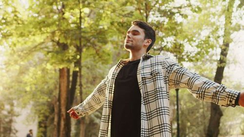 Man taking a deep breath in a sun-filled forest.