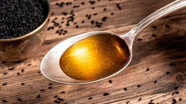 Löffel mit Schwarzkümmelöl vor einer Schüssel mit Schwarzkümmelsamen | Bild: mauritius images / Madeleine Steinbach / Alamy / Alamy Stock Photos