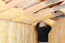 Worker Installing Fiberglass Batt Insulation between Roof Trusse