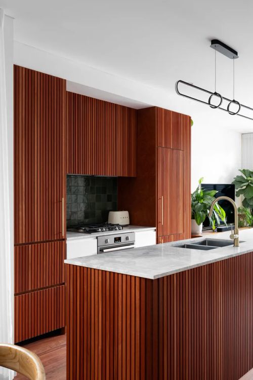 Modern kitchen with wood paneling, marble countertop, stainless steel appliances, and a plant.