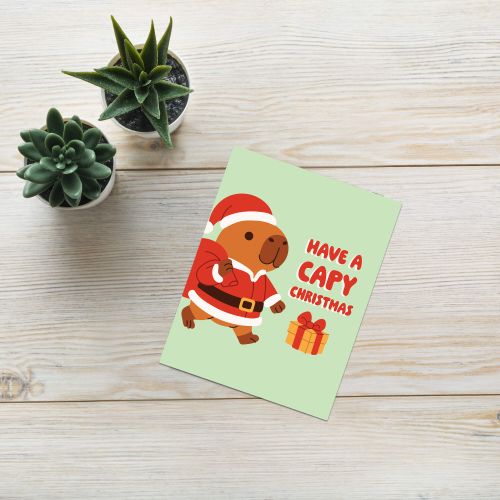cute unique Christmas card with a capybara in a Santa outfit and text 'Have a Capy Christmas' on a light green background.