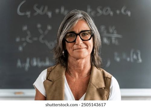 Mature female professor standing at college classroom looking at camera. Elegant School woman teacher Stock Photo