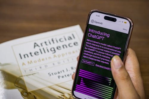 Free Close-up of a smartphone displaying ChatGPT app held over AI textbook. Stock Photo