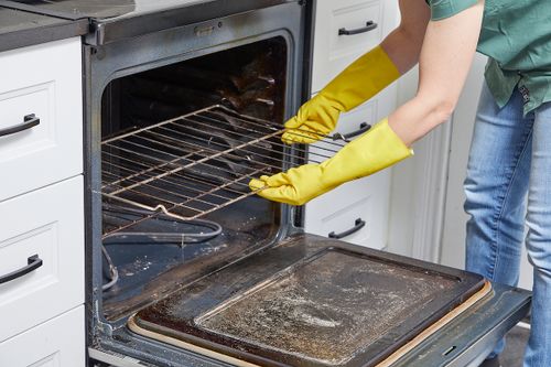 Woman wearing cleaning gloves removes oven racks for cleaning.