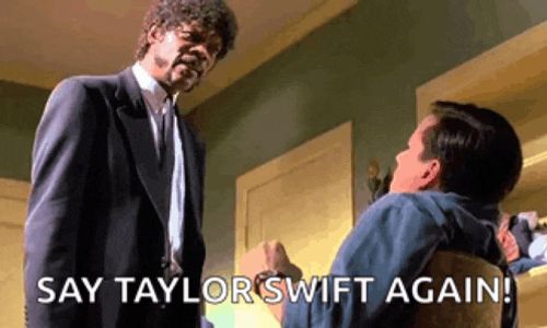 a man in a suit and tie is standing next to another man in a chair and saying " say taylor swift again " .