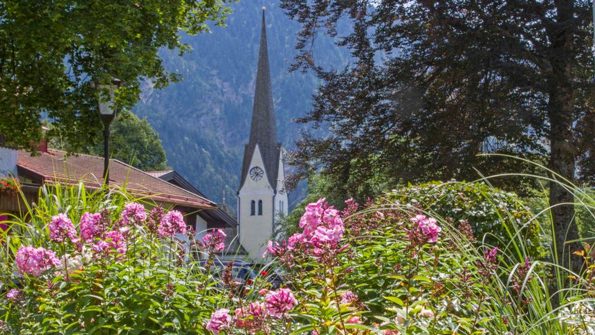 Die Kirche von Bayrischzell, im Vordergrund Büsche und rosafarbene Blumen