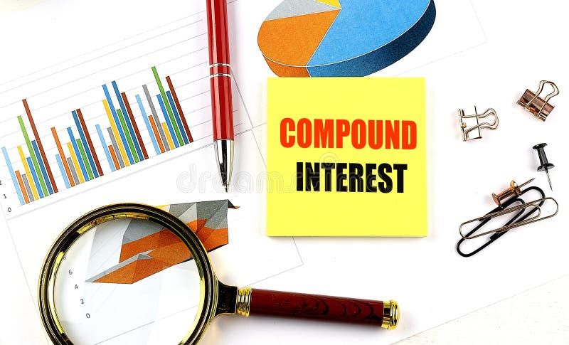 COMPOUND INTEREST text on yellow sticky on a chart with magnifier and pen .